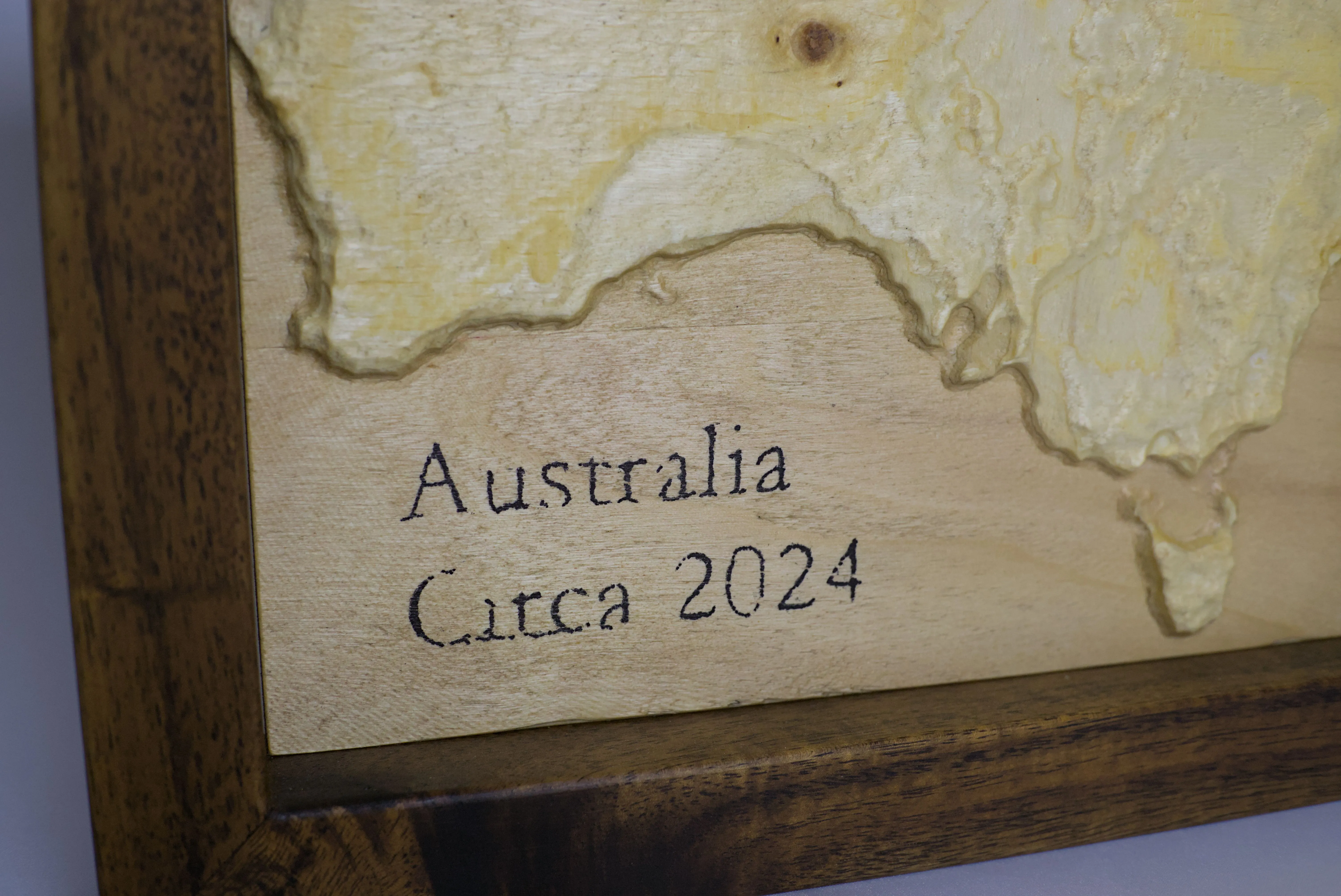A close up of the text "Australia Circa 2024" stamped into a timber 3D map of Australia.