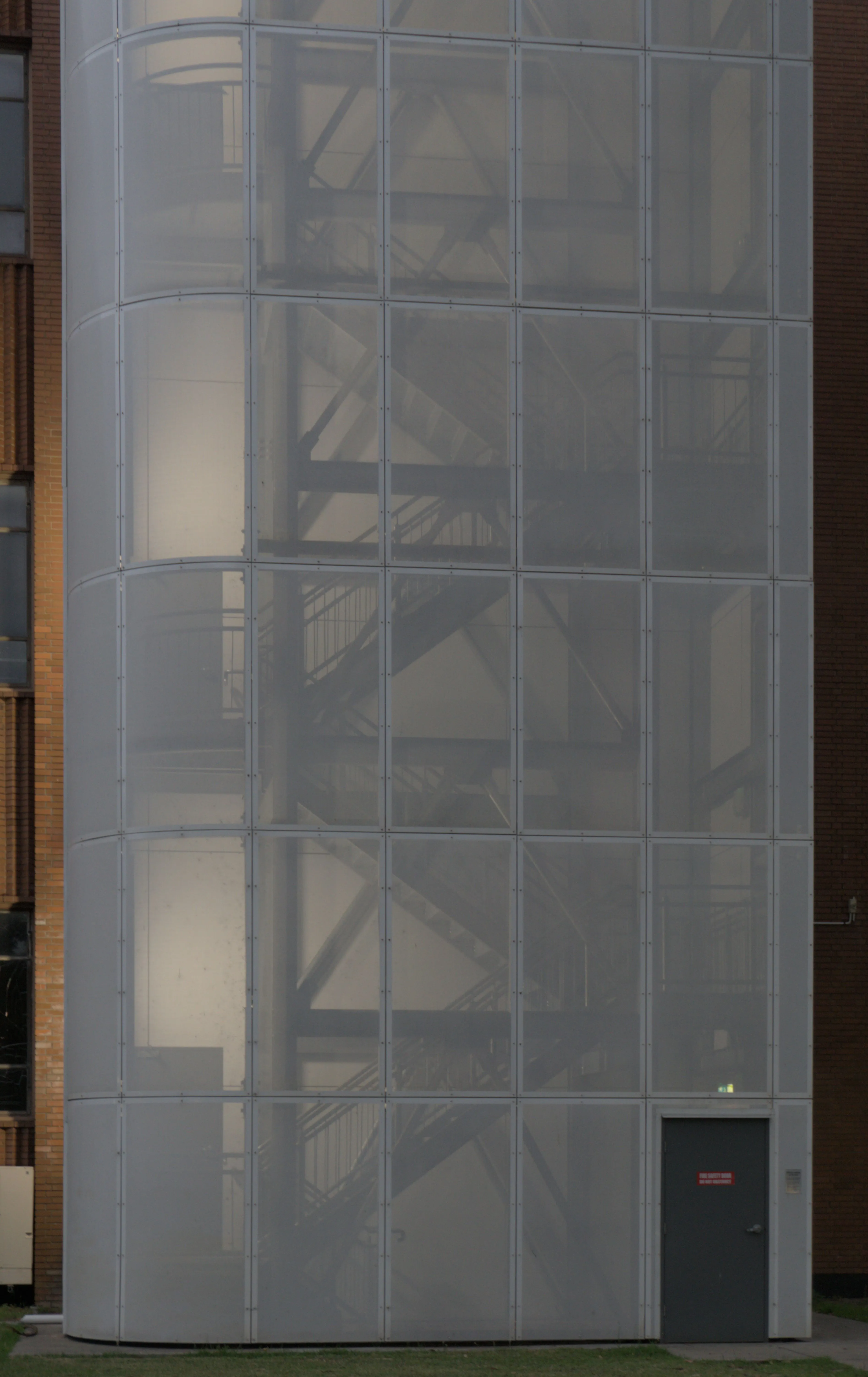 A lone green door leading into mesh covered fire escape stairs illuminated from inside at night